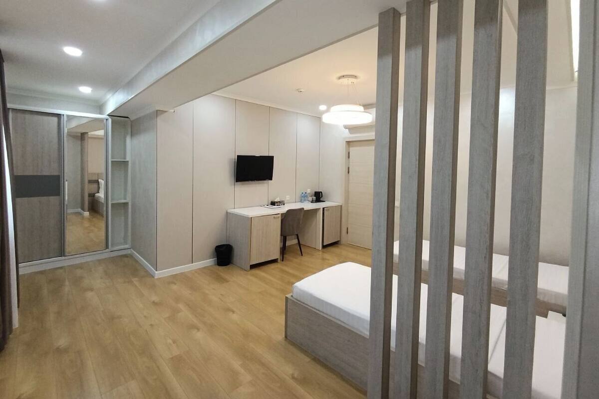 A modern hotel room with a wooden floor, a bed, a desk with a chair, a television, and a wardrobe.