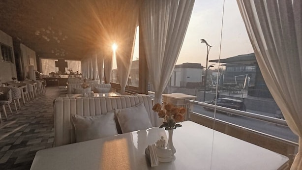 Une chambre d’hôtel dotée d’une grande fenêtre, d’un coin repas avec des tables et des chaises, et d’un canapé.