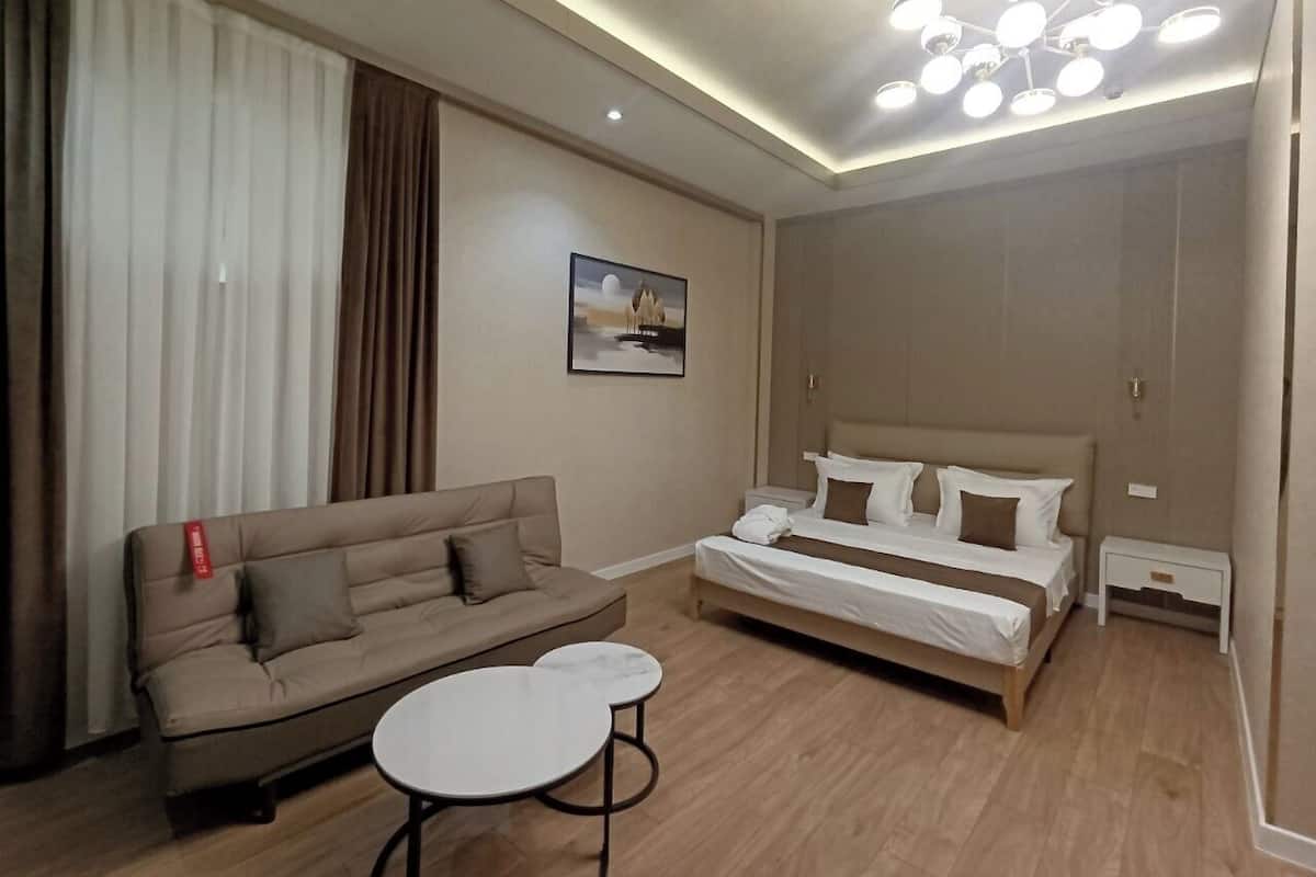A hotel room with a bed, a sofa, a small table, and a ceiling light fixture.