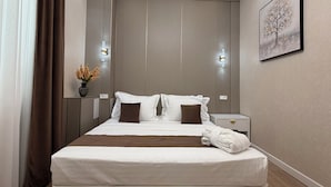 Une chambre d’hôtel moderne avec un grand lit, une table de chevet, un vase contenant des fleurs séchées et un tableau au mur.
