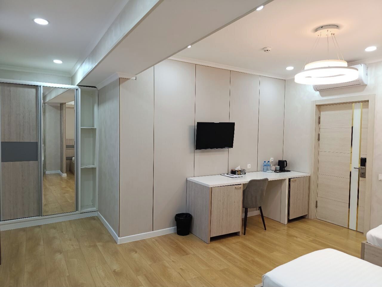 Una habitación de hotel moderna con suelo de madera, un escritorio con silla, un televisor de pantalla plana y una cama.