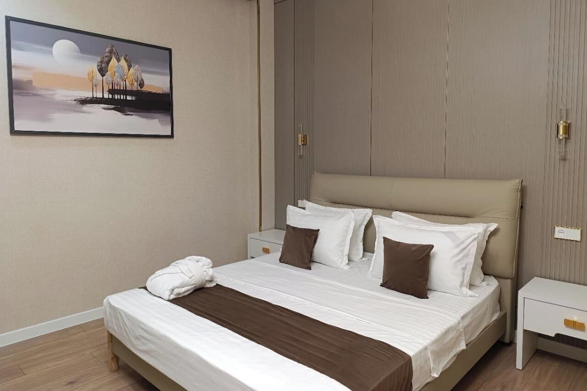 A hotel room with a large bed, a nightstand, a painting on the wall, and a wooden panel wall.