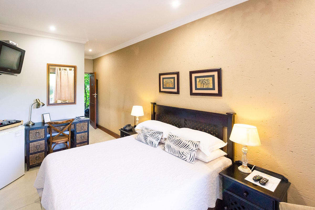 A hotel room with a bed, bedside lamps, a telephone, a television, and a wall-mounted picture frame.