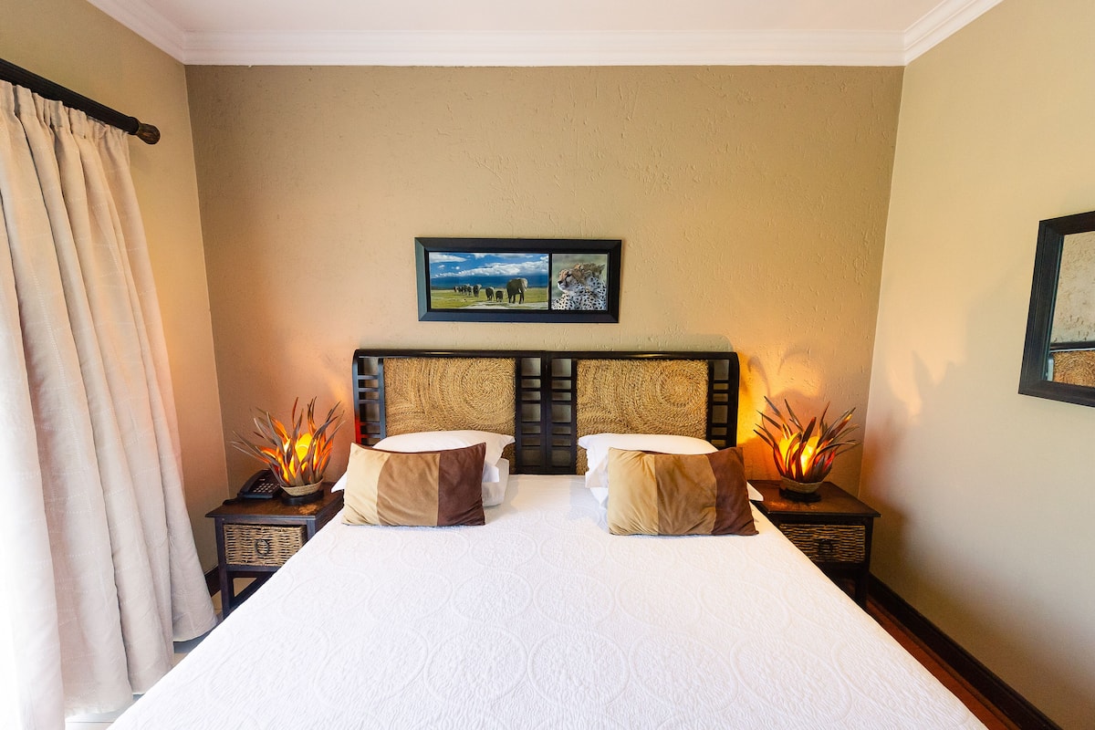 A double bed with a white bedspread, two bedside tables with lamps, and a framed picture above the bed.