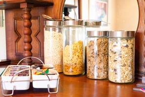 Four glass containers with metal lids on a wooden table, each filled with different types of grains and cereals.