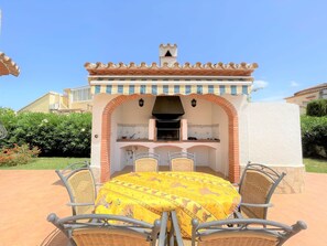 An outdoor patio with a round table and wicker chairs, a built-in grill, and a tiled backsplash. - T-0819, Villa Sueños, beautiful villa with mediterranean garden (Alicante)