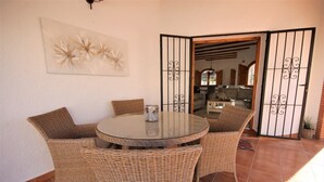 A wicker dining set with a glass table and chairs, a decorative wall piece, and a view into a room with a wooden ceiling and a gate. - T-0819, Villa Sueños, beautiful villa with mediterranean garden (Alicante)