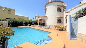 A swimming pool with lounge chairs and a patio area, surrounded by buildings with Mediterranean architecture. - T-0819, Villa Sueños, beautiful villa with mediterranean garden (Alicante)