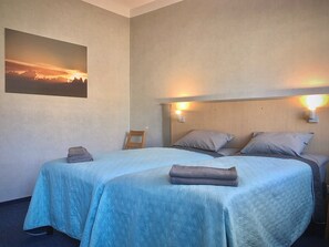 Habitación de hotel con dos camas, una mesita de noche, una silla y un cuadro de un atardecer en la pared.
