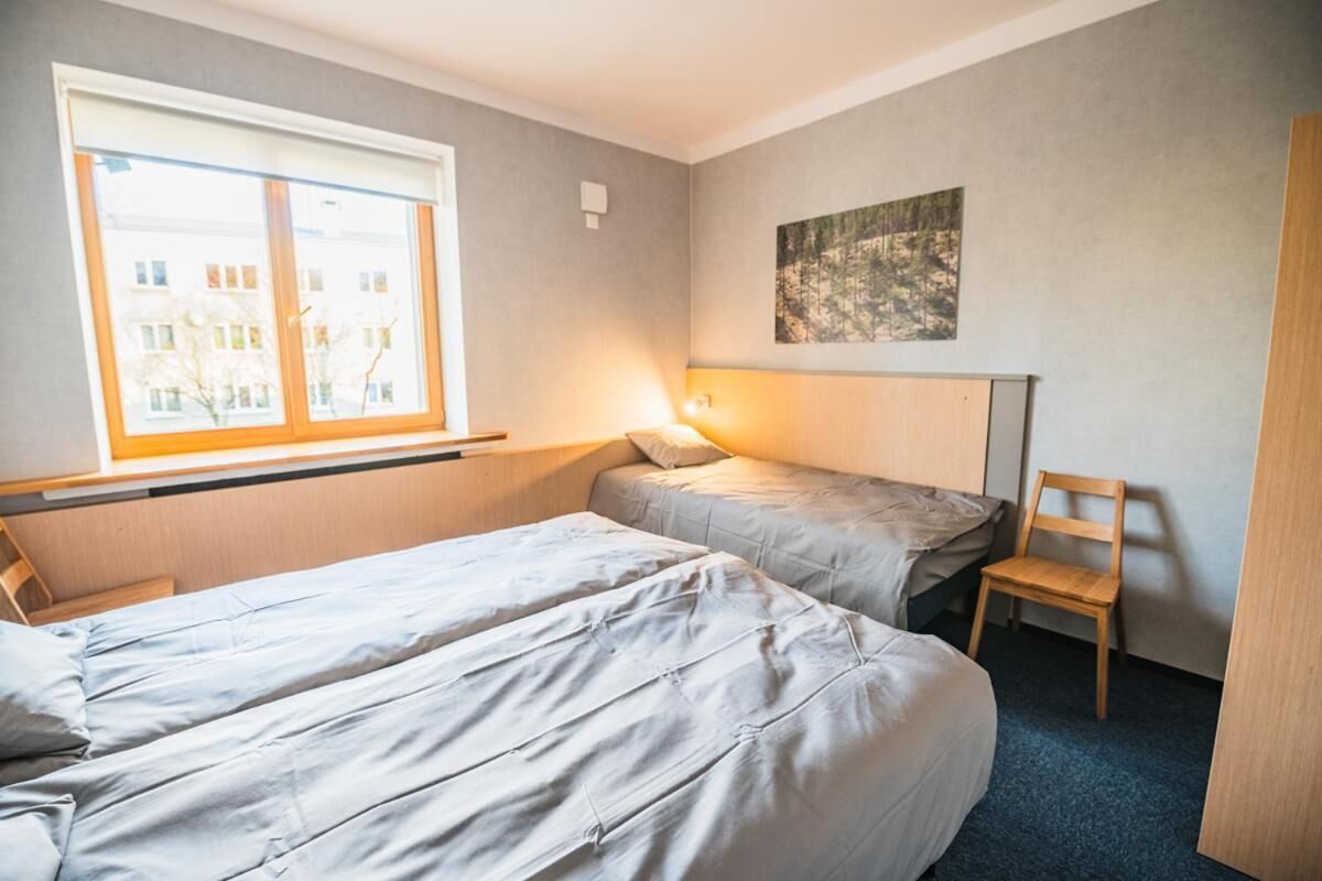 A hotel room with two beds, a window, a chair, and a painting on the wall.
