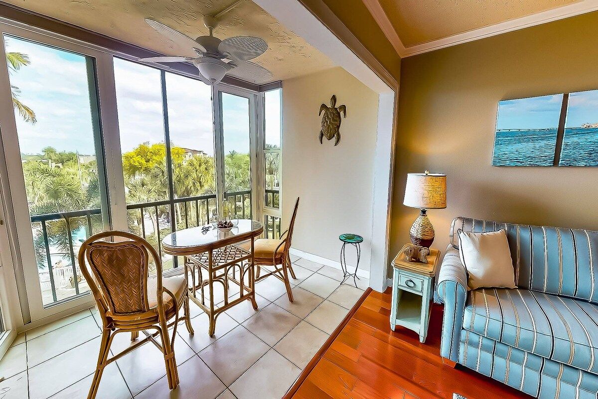 A room with a balcony, a dining table with chairs, a sofa, and a lamp.
