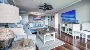 A living room with a sofa, coffee table, and TV. There is a ceiling fan and a painting on the wall. - Resort Style, Heated Pools plus Kiddie Pool, Walk to the Beach, On Bay, Tennis Courts (Siesta Key)