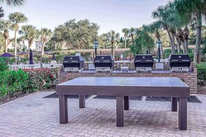 An outdoor patio with a brick barbecue area, a table, and surrounding greenery.