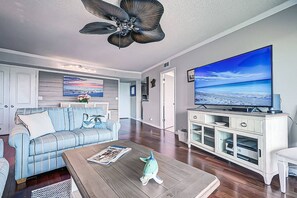A living room with a large flat-screen TV, a ceiling fan, and a sofa with striped cushions.