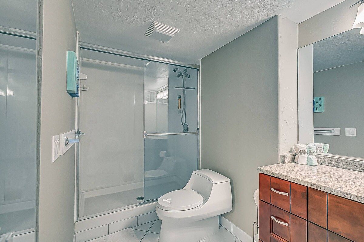 A bathroom with a glass-enclosed shower, a white toilet, and a wooden vanity with a marble countertop.