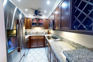 Cucina con elettrodomestici in acciaio inossidabile, mobili in legno, piano di lavoro in granito e ventilatore a soffitto.
