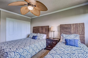 A bedroom with two beds, a ceiling fan, a nightstand with a lamp, and a door. - Resort Style, Heated Pool, Walk to Top Beach (Siesta Key)