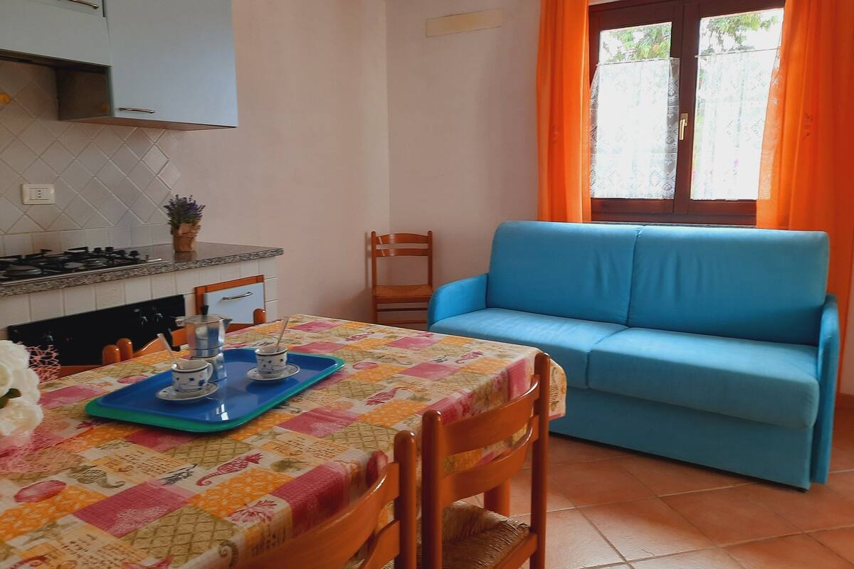 Una cocina con mesa y sillas, un sofá y una ventana con cortinas.