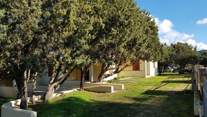 A building with a white exterior and a sloped roof, surrounded by trees and a grassy area. - Villette Sirenella (Aglientu)