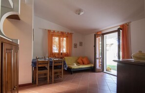 Una habitación con cama, una mesa con sillas, una ventana con cortinas y una puerta.