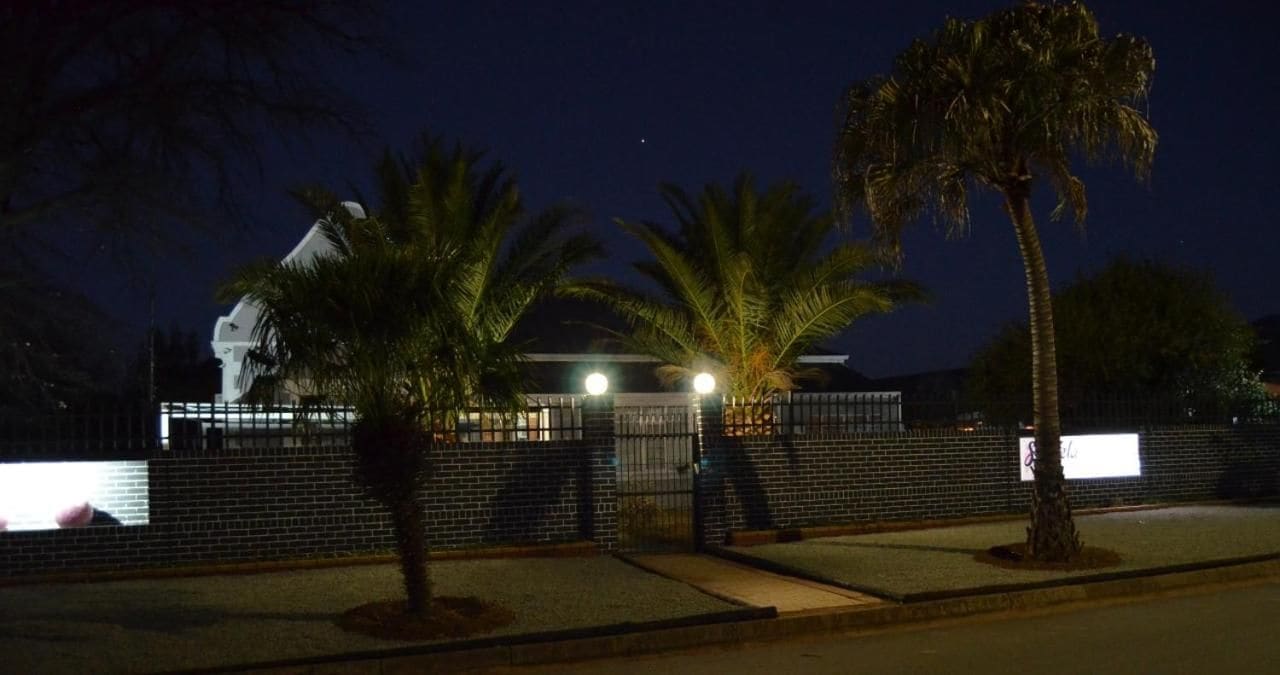 A gated area with palm trees and a building with a white roof at night.