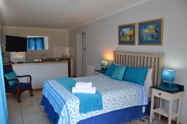 Una habitación de hotel con cama, escritorio, silla, televisor y obras de arte en la pared.