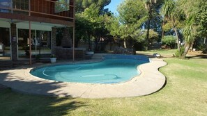 A swimming pool with a curved edge, surrounded by a concrete deck and a grassy area. - Sondela Bed and Breakfast (Maletswai)