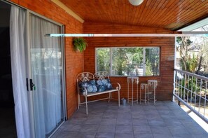 A wooden balcony with a bench and two small tables, a sliding glass door, and a view of greenery outside. - Sondela Bed and Breakfast (Maletswai)