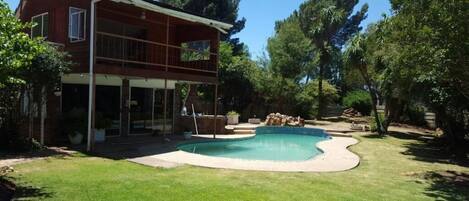 A two-story house with a swimming pool, surrounded by trees and a well-maintained lawn.