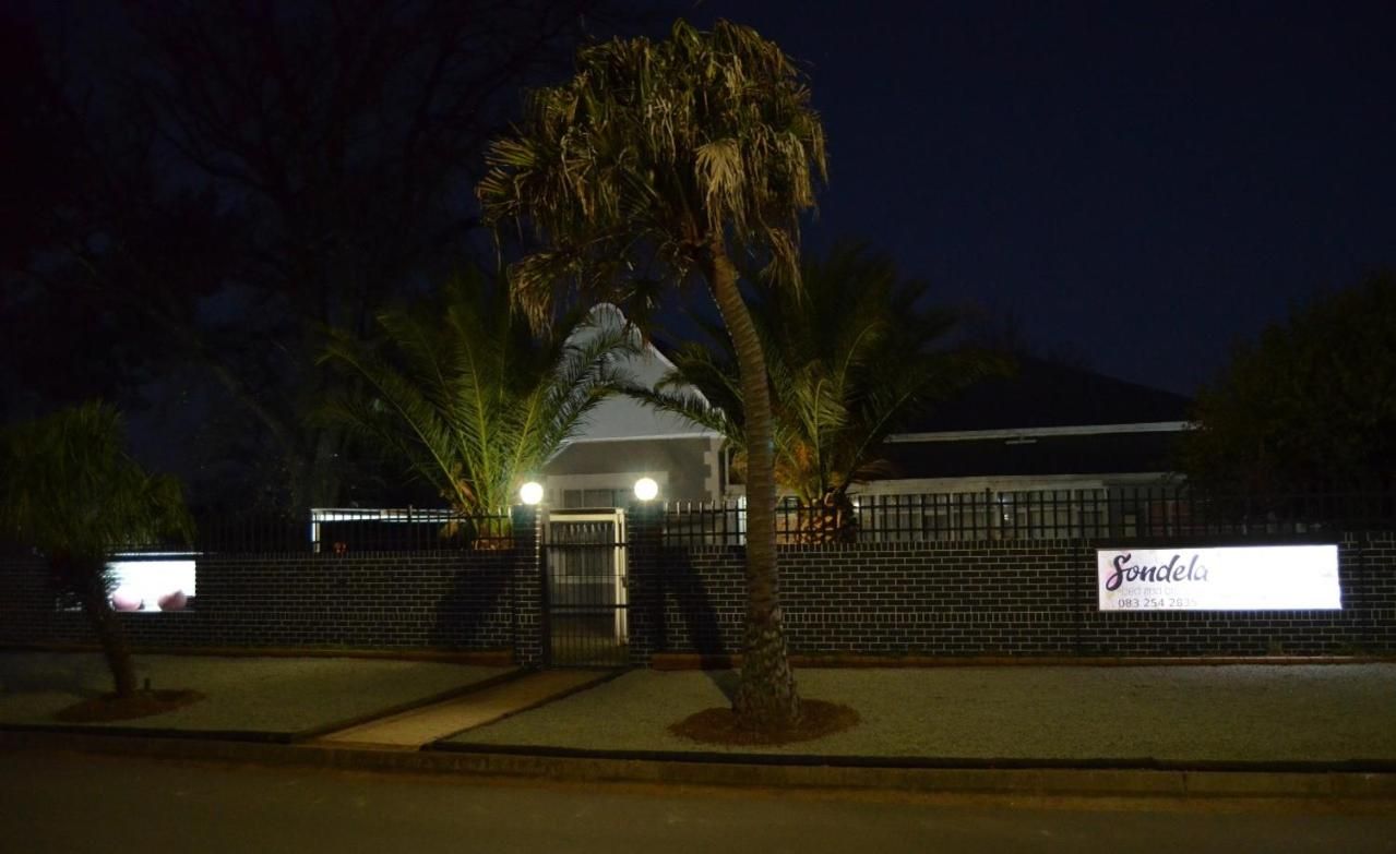 A building with a gated entrance, palm trees, and a signboard.