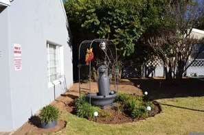 A building with a sign indicating parking at own risk, a fenced area with a birdcage sculpture, and a small garden with potted plants. - Sondela Bed and Breakfast (Maletswai)