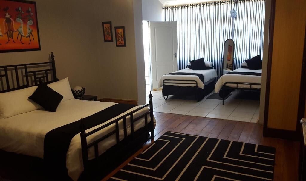 A hotel room with a large bed, two smaller beds, a black and white rug, and a door leading to another room.