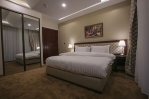 A hotel room with a large bed, a bedside table with a lamp, a mirror, and a painting on the wall.