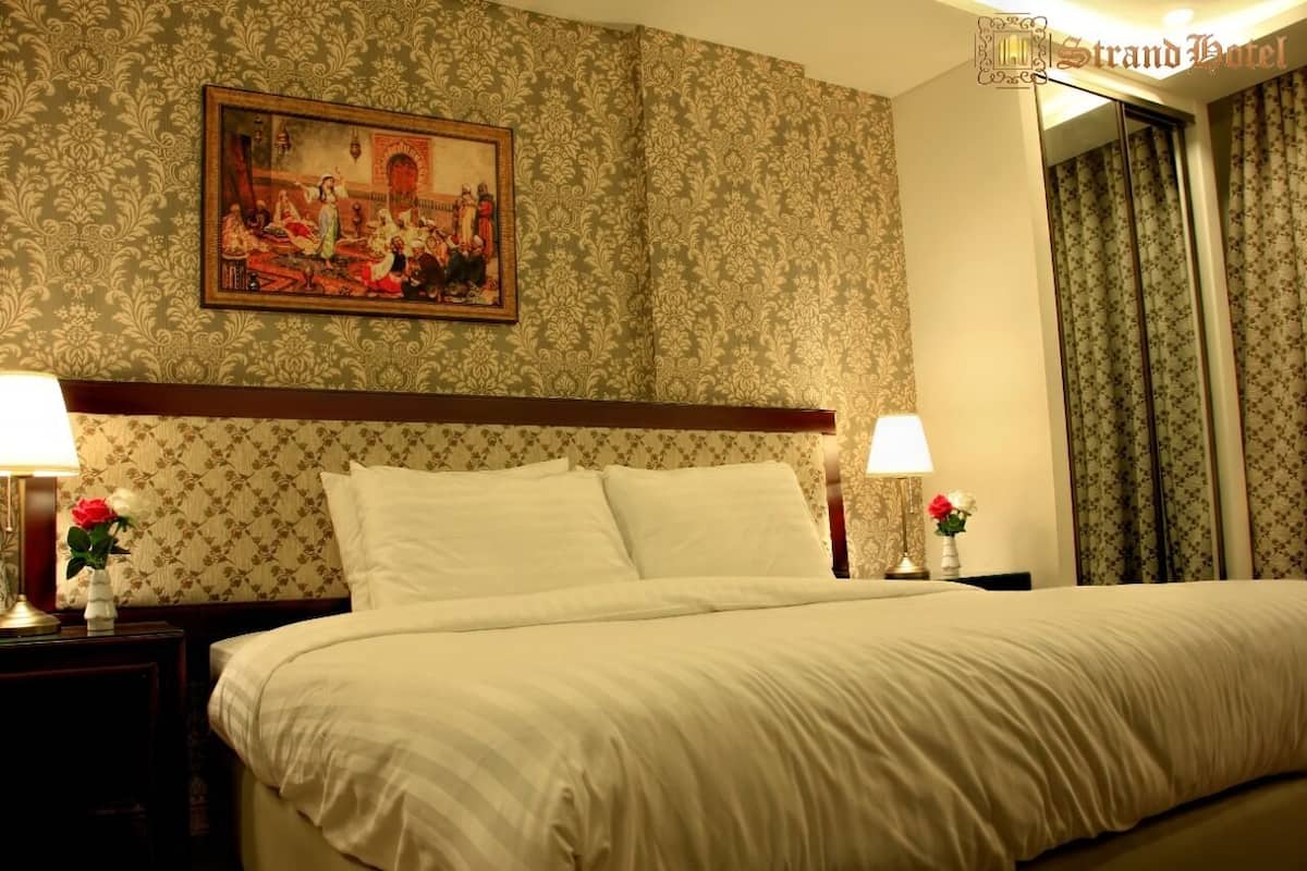A hotel room with a large bed, two bedside tables with lamps, a floral-patterned wallpaper, and a framed picture on the wall.