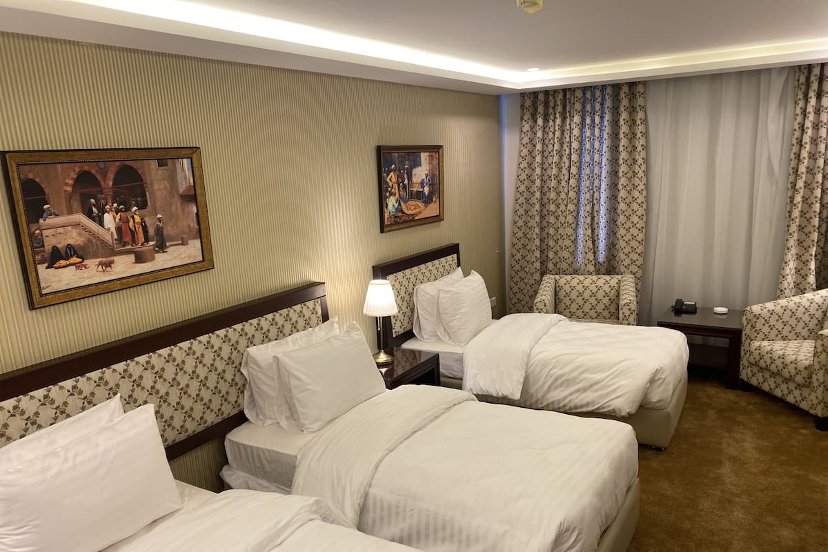 A hotel room with three beds, a nightstand, a lamp, and two chairs.