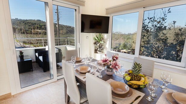 A dining area with a table set for four, a fruit bowl, and a flat-screen TV mounted on the wall. - Creta  Galini  House (Chania Creta)