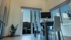 A dining area with a wooden ceiling, a table with chairs, a television, and a view through a glass door. - Creta  Galini  House (Chania Creta)