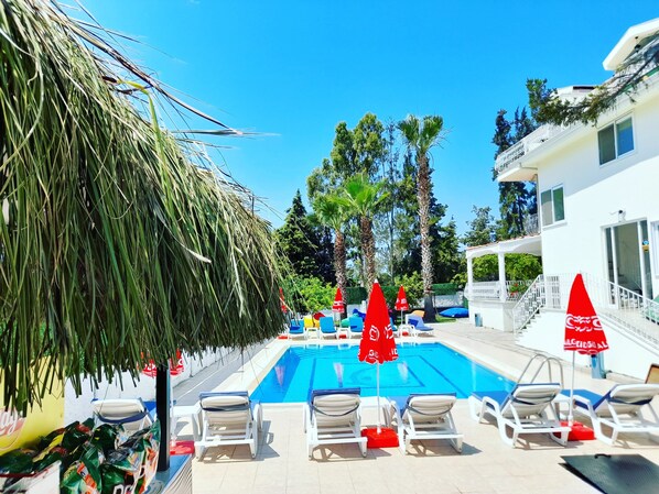 A swimming pool with lounge chairs and umbrellas, surrounded by palm trees and a white building. - Infinity Ruby Hotel (Fethiye)