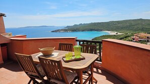A terrace with a table, chairs, and a view of the sea and hills. - Le Residenze La Marmorata (Santa Teresa di Gallura)