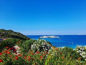 Paisatge costaner amb una vista clara del mar, roques i un vehicle vermell aparcat a prop d'un camí.