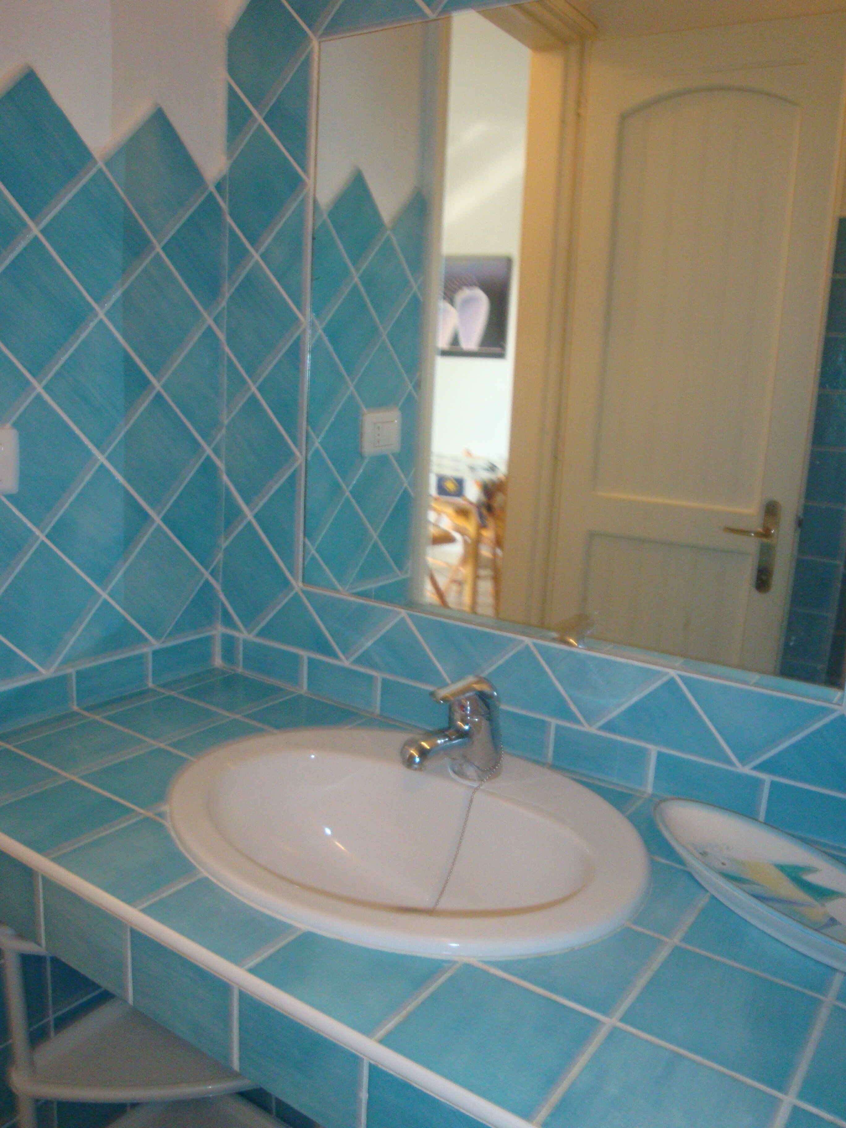 A bathroom with a sink, mirror, and blue-tiled walls.