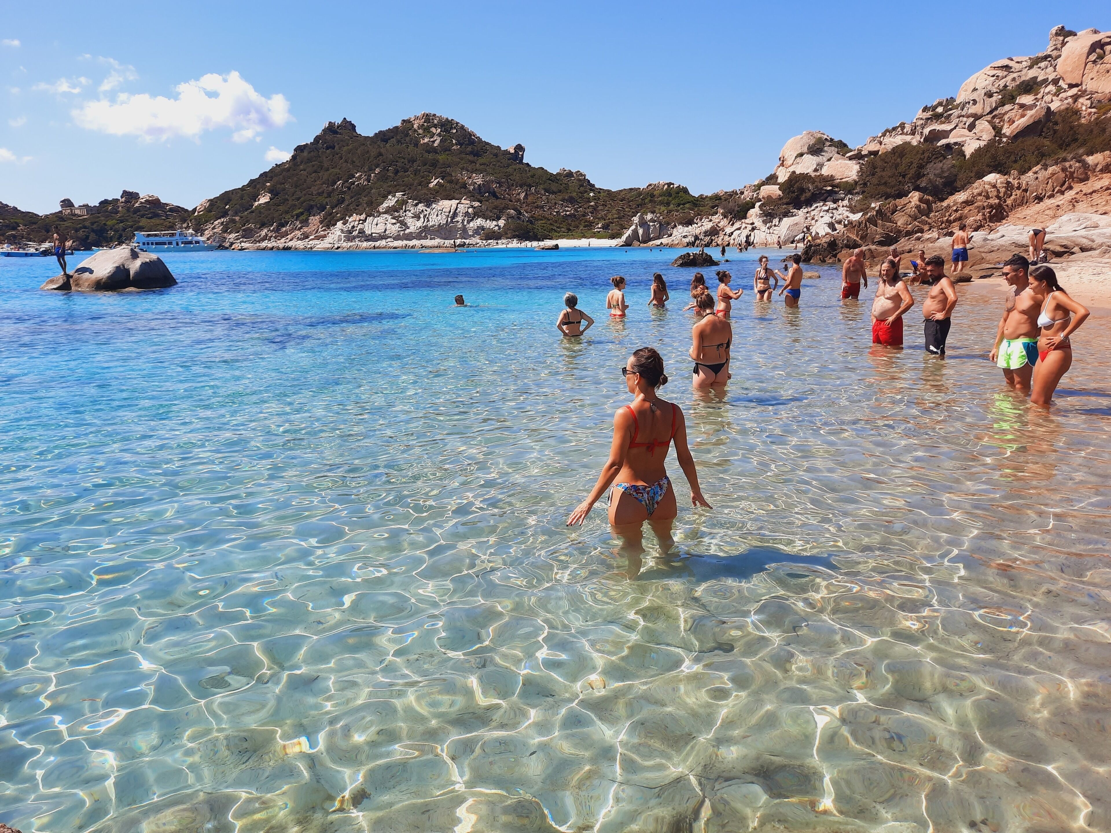 A beach with clear water and rocky hills in the background.