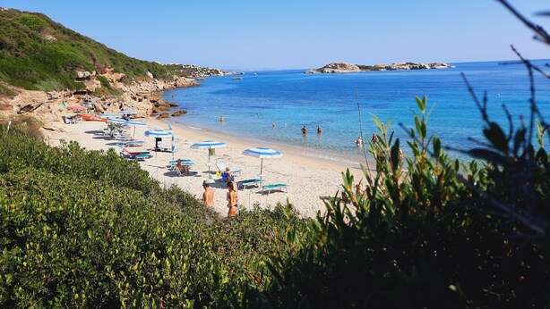 Une plage avec une eau d’un bleu limpide, des falaises rocheuses et quelques parasols.