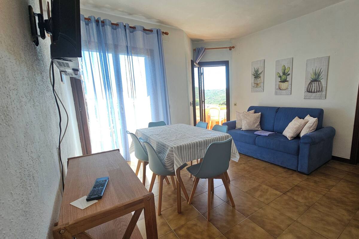 A living room with a blue sofa, a dining table with chairs, and a TV mounted on the wall.