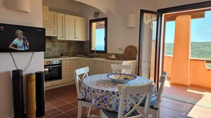 A kitchen with white cabinets, a TV mounted above the counter, and a dining area with a table and chairs. - Le Residenze La Marmorata (Santa Teresa di Gallura)