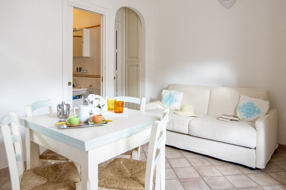 A dining area with a white table and chairs, a white sofa, and a tiled floor.