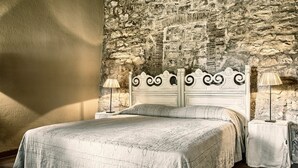 Ein Schlafzimmer mit Steinwand, einem Bett mit weißem Kopfteil, zwei Nachttischen mit Lampen und einem großen Fenster, das Licht auf das Bett wirft.