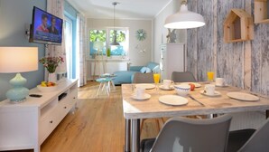 A modern dining area with a table set for four, a television mounted on the wall, and a rustic wooden wall. - Florida app. 2 Tuesday (Ostseebad Boltenhagen)