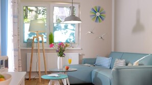 A modern living room with a blue sofa, a small round table, a lamp, and a window with a view. - Florida app. 2 Tuesday (Ostseebad Boltenhagen)