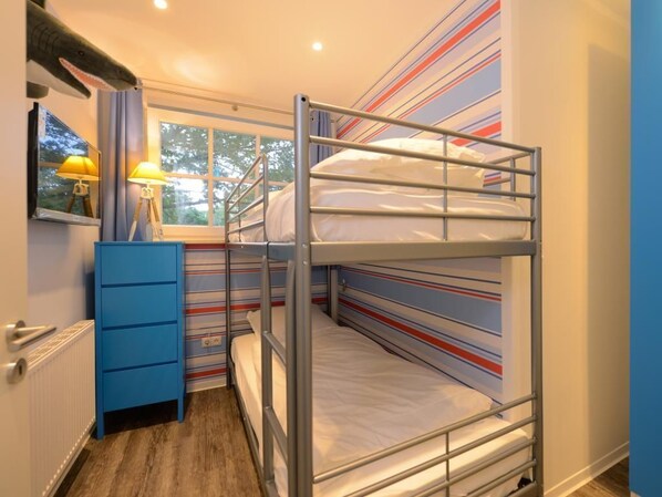 Une chambre avec un lit superposé, du papier peint à rayures, une commode bleue et deux lampes.